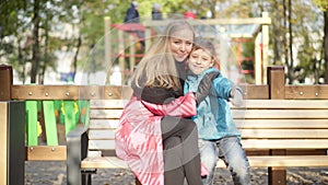 Portrait of cheerful woman and boy hugging showing thumbs up smiling looking at camera in sunlight. Happy Caucasian