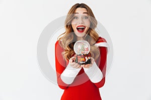 Portrait of cheerful woman 20s wearing Santa Claus red costume smiling and holding Christmas snow ball, isolated over white