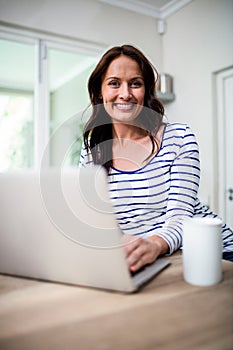 Portrait of cheerful woman working on laptop while holding coffee mug