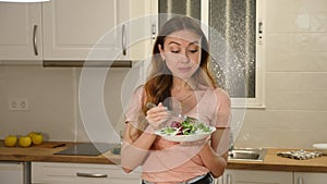 Portrait of cheerful young adult woman eating vegetable salad in home kitchen