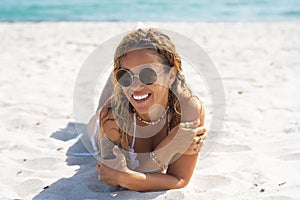 Portrait of cheerful young adult woman laying at the beach on white sand. Tropical summer holiday vacation. Relaxed female people