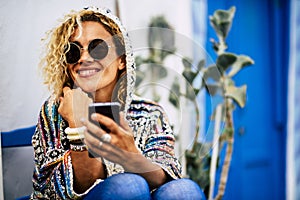 Portrait of cheerful young adult woman wearing circular sunglasses and smiling using smart phone connection outdoor home - happy