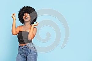 Portrait of cheerful young African American female model in black top and jeans, with afro hairstyle, smiling to the camera. Real