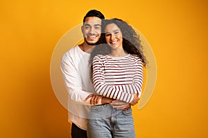 Portrait of cheerful young arab couple embracing and smiling at camera