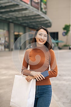 Portrait of cheerful young Asian woman with shopping bags at outdoor mall