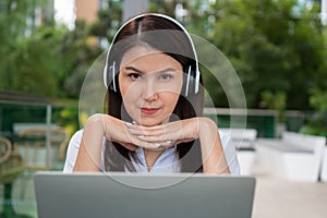 Portrait of a cheerful young attractive Asian woman listening music and using laptop computer for working online. Distance