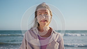 Portrait of cheerful young blonde woman smiling with white teeth at ocean beach