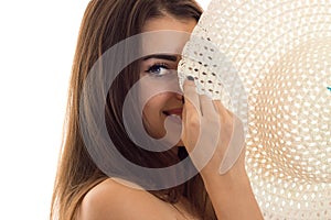 Portrait of cheerful young brunette girl with straw hat in her hands smiling on camera isolated on white background