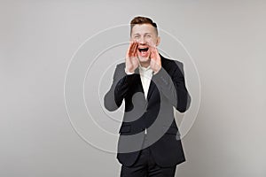 Portrait of cheerful young business man in classic black suit, shirt screaming with hand gesture isolated on grey