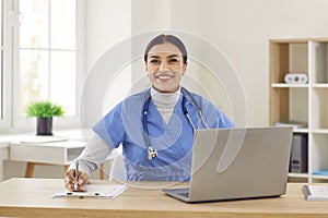 Portrait of cheerful young friendly female doctor in blue medical uniform looking at camera.