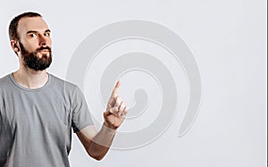 Portrait of cheerful young handsome man smiling looking at camera pointing finger upwards on white background with space for