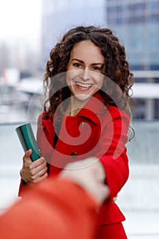 Portrait of a cheerful young happy women in red suit, greet by hand, on the property business background.