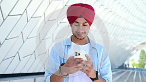 Portrait of cheerful young Indian guy sending message on mobile phone outdoors.