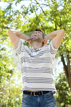 Young man laughing outdoors with his hands behind head