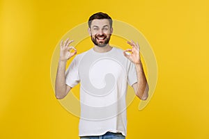 Portrait of a cheerful young man showing okay gesture isolated on yellow background