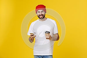 Portrait of a cheerful young man wearing casual clothes standing isolated over yellow background, holding mobile phone