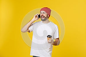 Portrait of a cheerful young man wearing casual clothes standing isolated over yellow background, holding mobile phone