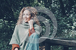 Portrait of cheerful young mature woman smiling and enjoying outdoor leisure activity sitting at the park with green trees and