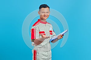 Portrait of a cheerful young mechanic holding clipboard and pointing with palm at camera isolated on blue background