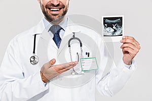 Portrait of cheerful young medical doctor working in hospital and holding ultrasound scan of baby