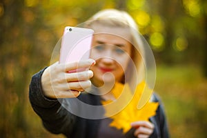 Portrait of cheerful young woman with autumn leafs in front of foliage making selfie