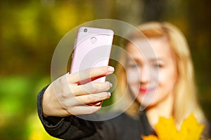 Portrait of cheerful young woman with autumn leafs in front of foliage making selfie