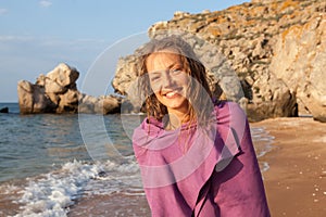 Portrait of a cheerful young woman on the beach wrapped in a towel