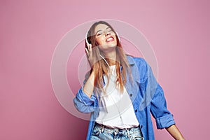 Portrait of cheerful young woman with headphones listening to music on a colorful pink background