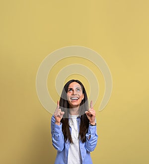 Portrait of cheerful young woman pointing upwards towards copy space against yellow background. Beautiful female with long hair