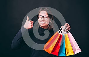 Portrait of cheerful young woman showing thumb up and holding colorful shopping bags