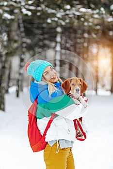 Portrait of cheerful young woman in warm stylish clothes and bagpack posing with her beagle dog in winter park