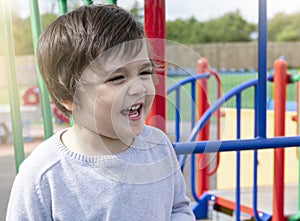 Portrait of cheerfull little boy having fun on playground outdoors, Cute 3 year old boy excited plays on a colourful playground on