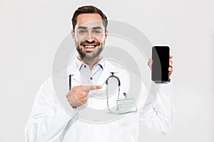 Portrait of cheery young medical doctor with stethoscope working in clinic and holding cellphone