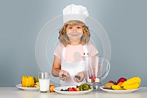 Portrait of chef child in cook hat cooking blueberries smoothie. Cooking at home, kid boy preparing food from vegetable