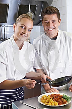 Portrait Of Chef Instructing Female Trainee In Restaurant Kitchen