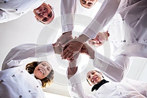 Portrait of chefs team putting hands together and cheering