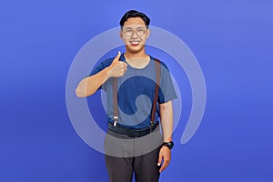 Portrait of cherful Asian man showing thumbs up or sign of approval isolated on purple background