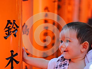 Portrait of a cherful little baby with red colorful toriis of Fushimi Inari Taisha shrine on background. photo