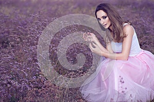 Portrait of chic woman with provocative make up and long hair sitting in the field of violet flowers.