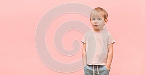 Portrait of a child of a 3 years old blond boy looking surprised at the camera on a pink background with place for text