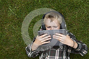 Portrait of Child blond young boy playing with a digital tablet computer outdoors lying on grass