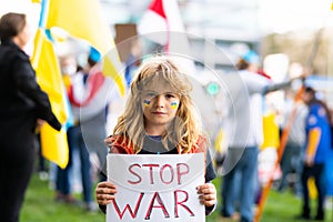 Portrait of child boy calls to Stop war in Ukraine, holding a poster with Stop the war message standing outdoor. Russian