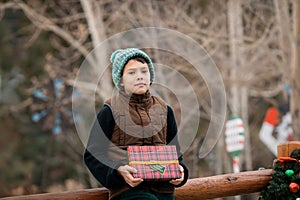 Portrait of child boy with Christmas gift box standing outside and looking at camera, childhood memories and season holidays