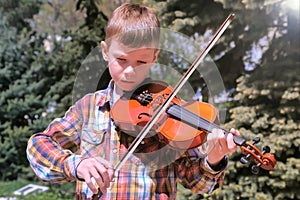Portrait of child boy is playing the violin standing in park.