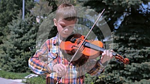 Portrait of child boy is playing the violin standing in park.