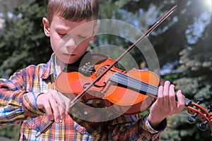 Portrait of child boy is playing the violin standing in park on pine background.