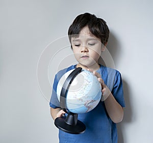 Portrait child boy standing next to the wall looking  a globe  with curious face, Selective focus School kid Child boy learning