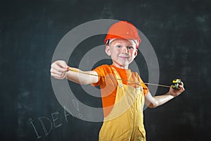 Portrait of child dressed as builder with ruller in hands. Little boy wearing hard ptotect helmet. Little builder in