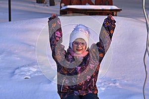 Portrait of a child girl in glasses on a sunny winter evening. The girl enjoys the evening walk. The girl`s face is lit by the ra