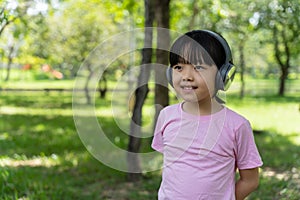 Portrait of child girl listens to music with modern headphones in park outdoors.